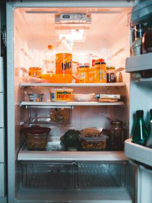 Jars with drinks and containers with preserved food on shelves in fridge at home